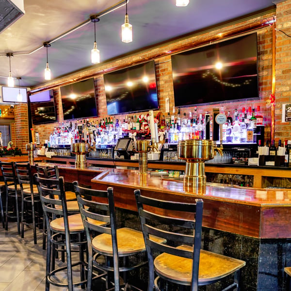 Austin's Ale House bar with stools, brick walls, multiple TVs, and a well-stocked liquor display.