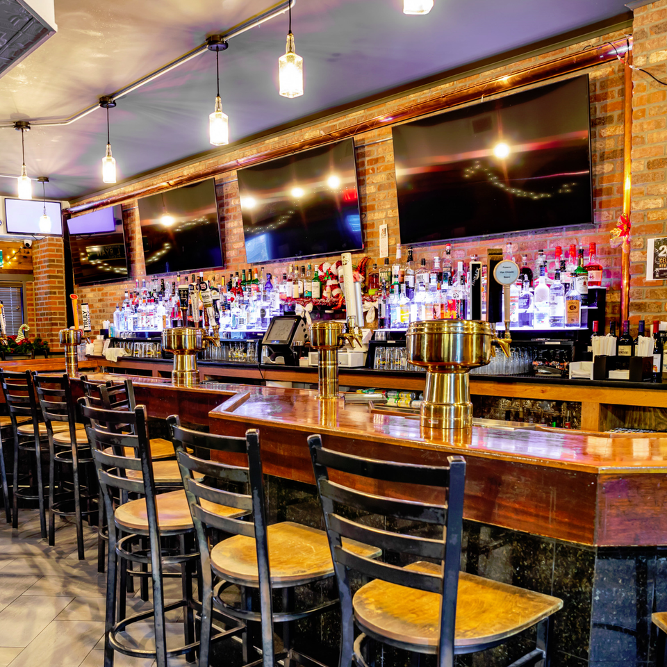 Austin's Ale House bar with stools, brick walls, multiple TVs, and a well-stocked liquor display.