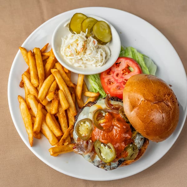 Austin's Ale House burger with fries, coleslaw, pickles, lettuce, and tomato on a white plate.