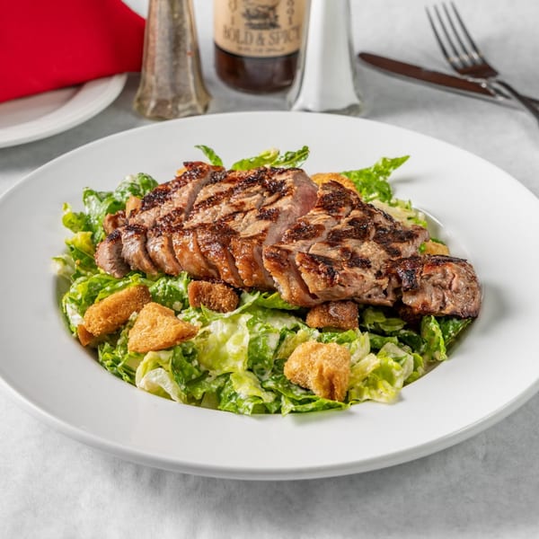 Grilled steak Caesar salad with croutons on a white plate at Austin's Ale House.