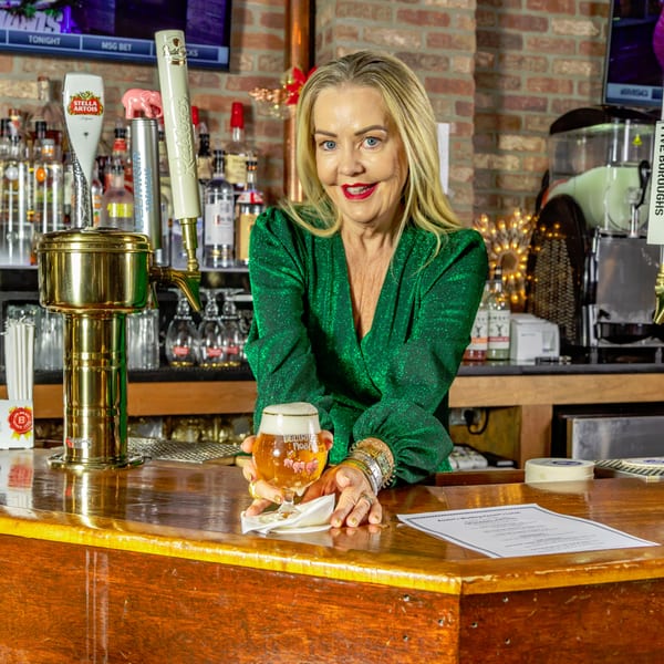 A woman in a green dress smiles, holding a beer at the Austin's Ale House bar.