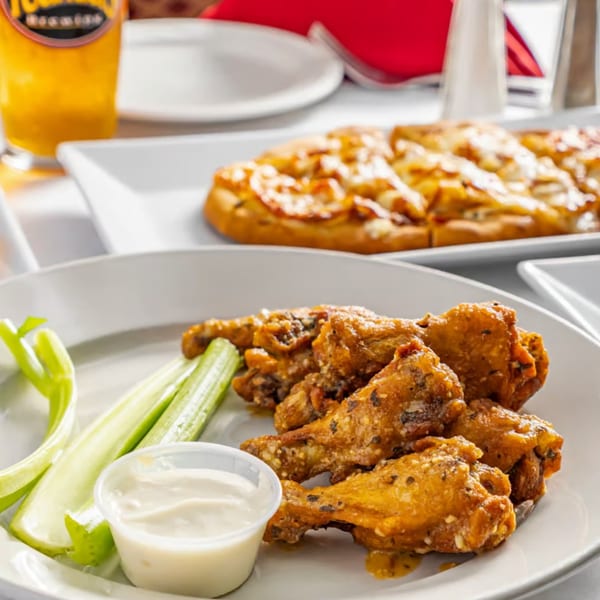 Austin's Ale House wings with celery and dipping sauce, with a flatbread and beer in the background.