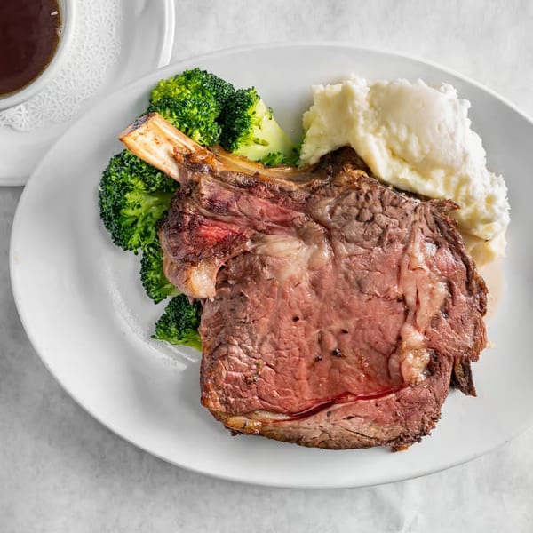 Austin's Ale House prime rib with bone, mashed potatoes, and broccoli on a white plate.
