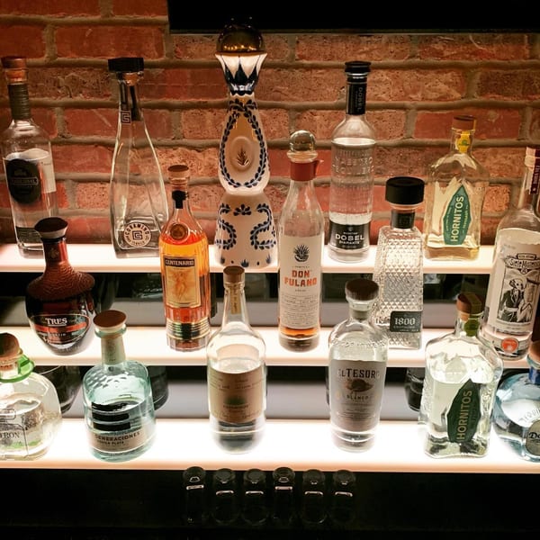 A backlit display of various tequila bottles, including Don Fulano and Hornitos, against a brick wall.