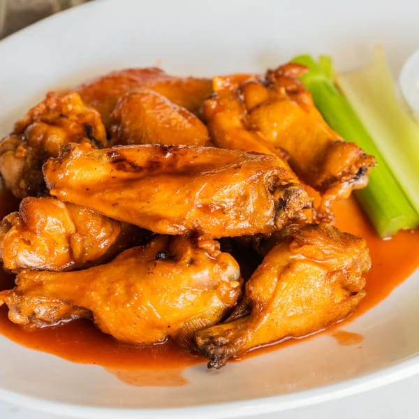 Austin's Ale House buffalo wings, coated in orange sauce, with celery sticks on a white plate.
