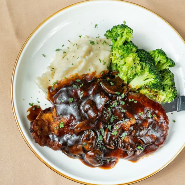 Chicken fried steak with mushroom gravy, mashed potatoes, and broccoli on a white plate.