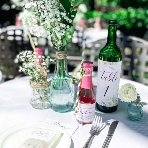 Outdoor table setting with floral centerpieces, a mini champagne bottle, and a "Table 1" sign.