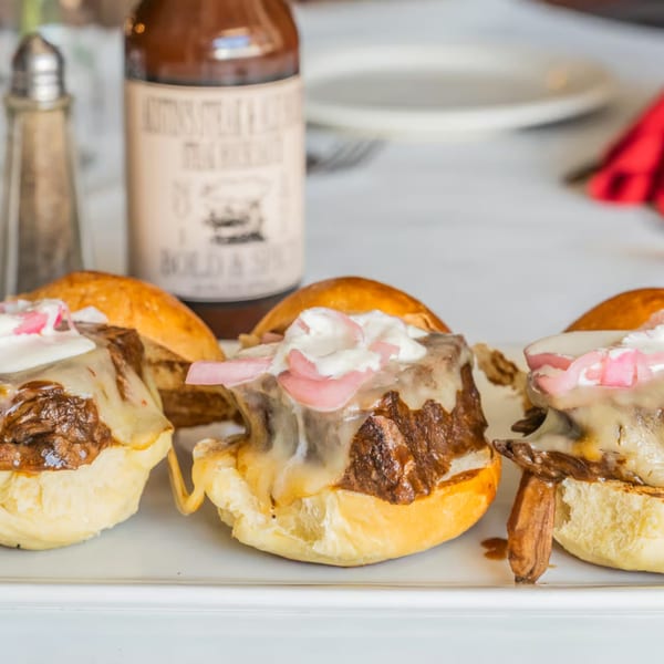 Three Austin's Ale House sliders with melted cheese, meat, sour cream, and pickled onions.