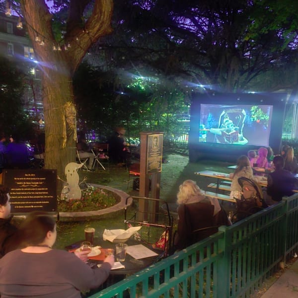 Patrons enjoying an outdoor movie night at Austin's Ale House, with a large screen showing a cartoon.