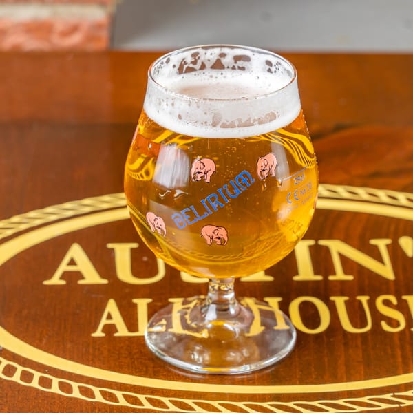 A glass of Delirium beer with pink elephants on a wooden table with Austin's Ale House logo.
