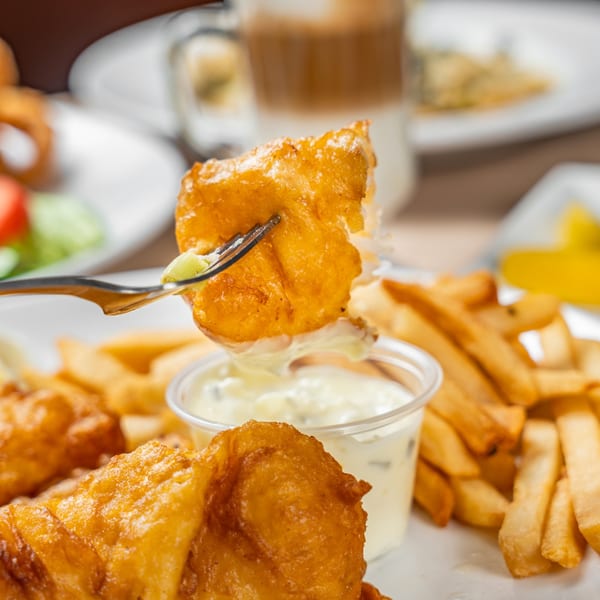Golden-brown fish and chips with tartar sauce, a fork lifting a piece of fish.
