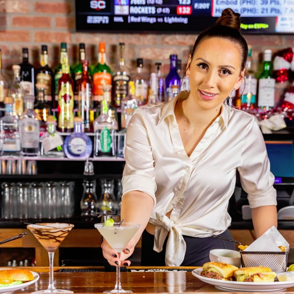 Bartender at Austin's Ale House serving a margarita, with sliders and another cocktail on the bar.