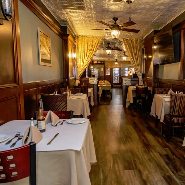 Long, narrow dining room with set tables, wood paneling, ceiling fans, and gold curtains.